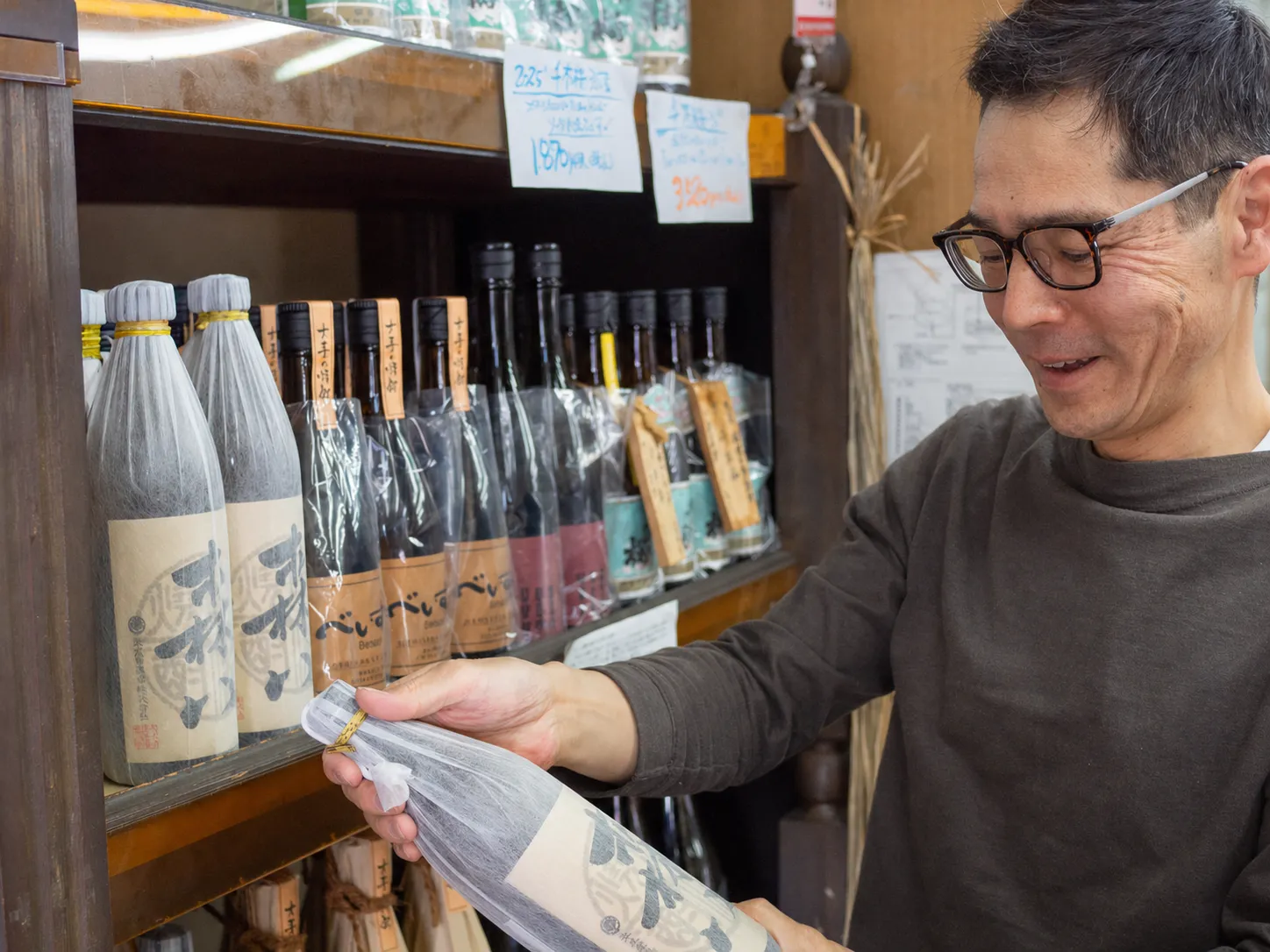 棚に並ぶ酒を手に取る松石酒店の店主